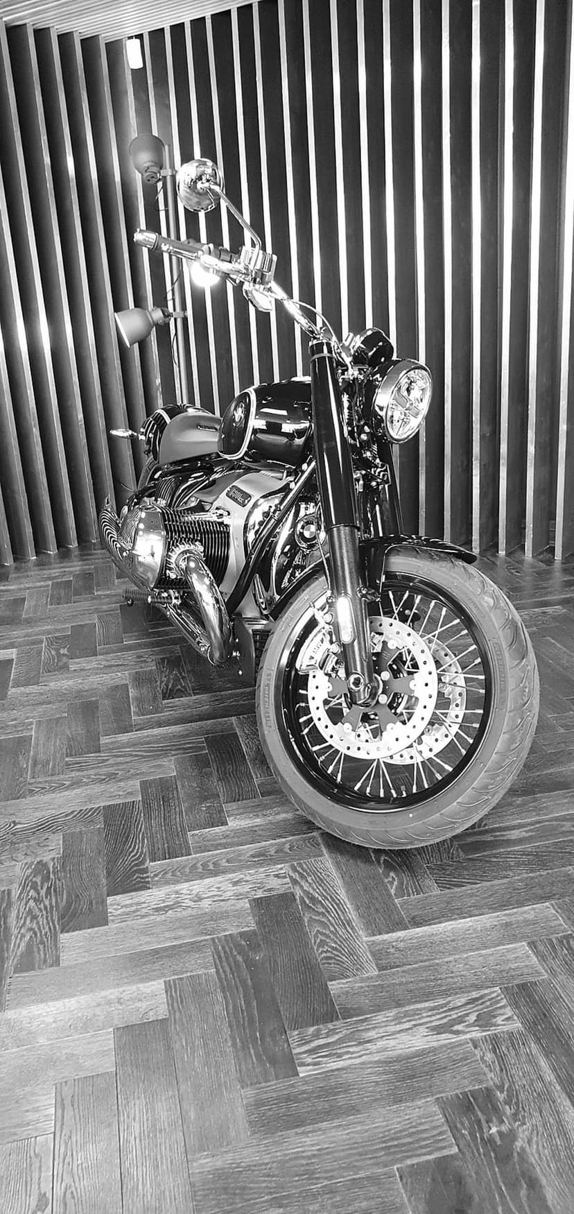Vintage chrome motorcycle with polished engine components parked on a dark herringbone patterned wooden floor.