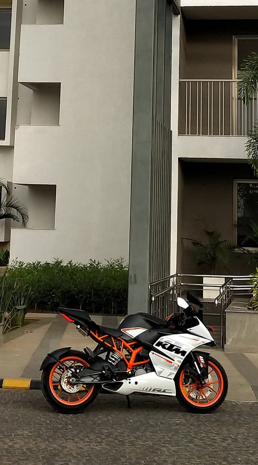 KTM RC motorcycle with orange and white fairings parked on pavement near a modern building with green plants.