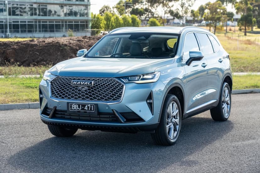 Light blue Haval SUV parked on asphalt with a modern building and green trees in the background.