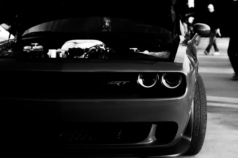 Dodge Challenger SRT Hellcat with an open hood and exposed engine in a dramatic black and white front view.