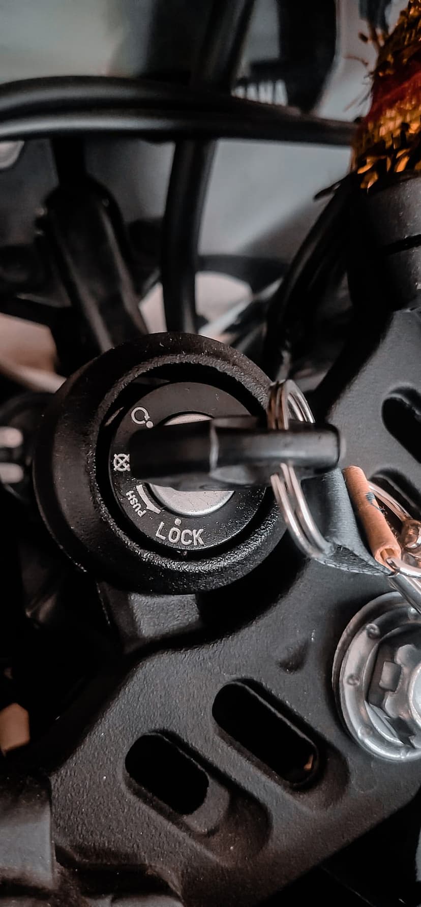 Metal motorcycle key partially inserted into a chrome ignition lock with engraved LOCK and PUSH lettering.