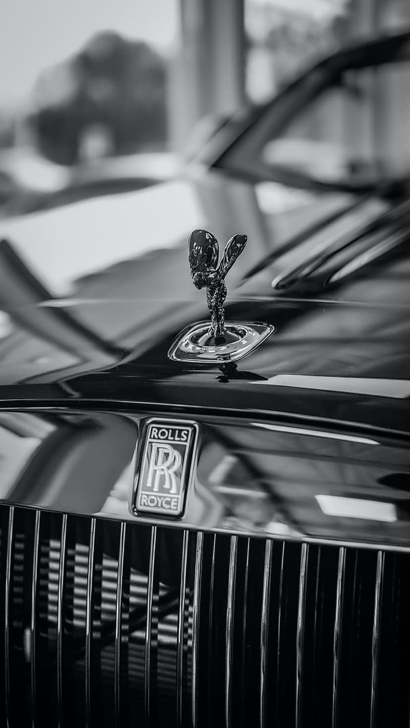 Spirit of Ecstasy hood ornament stands on a vertical metal grille in a high-contrast monochrome photograph.
