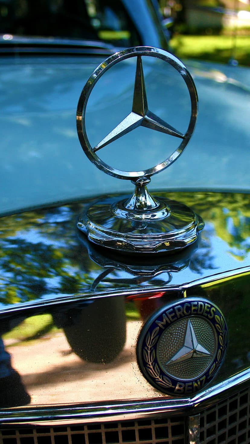 Mercedes-Benz three-pointed star hood ornament in polished chrome reflecting light on a classic car hood.