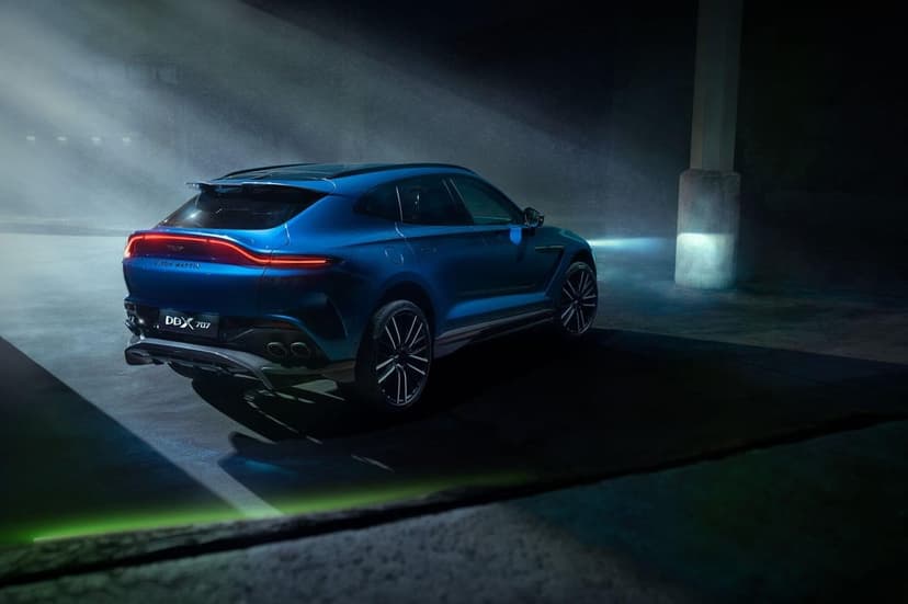 Blue Aston Martin DBX 707 luxury SUV with glowing red taillights in a dark foggy industrial garage.