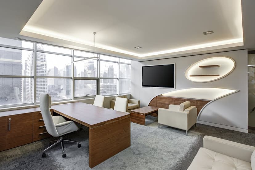 Executive desk and beige armchairs overlook a sprawling urban skyline through massive floor-to-ceiling windows.