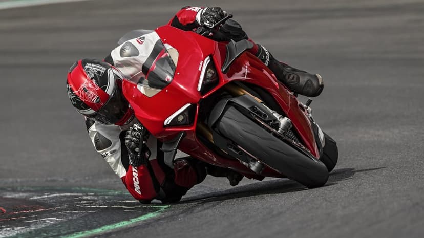 Red Ducati sportbike leans deep into a racetrack corner with a rider dragging knee on the asphalt.