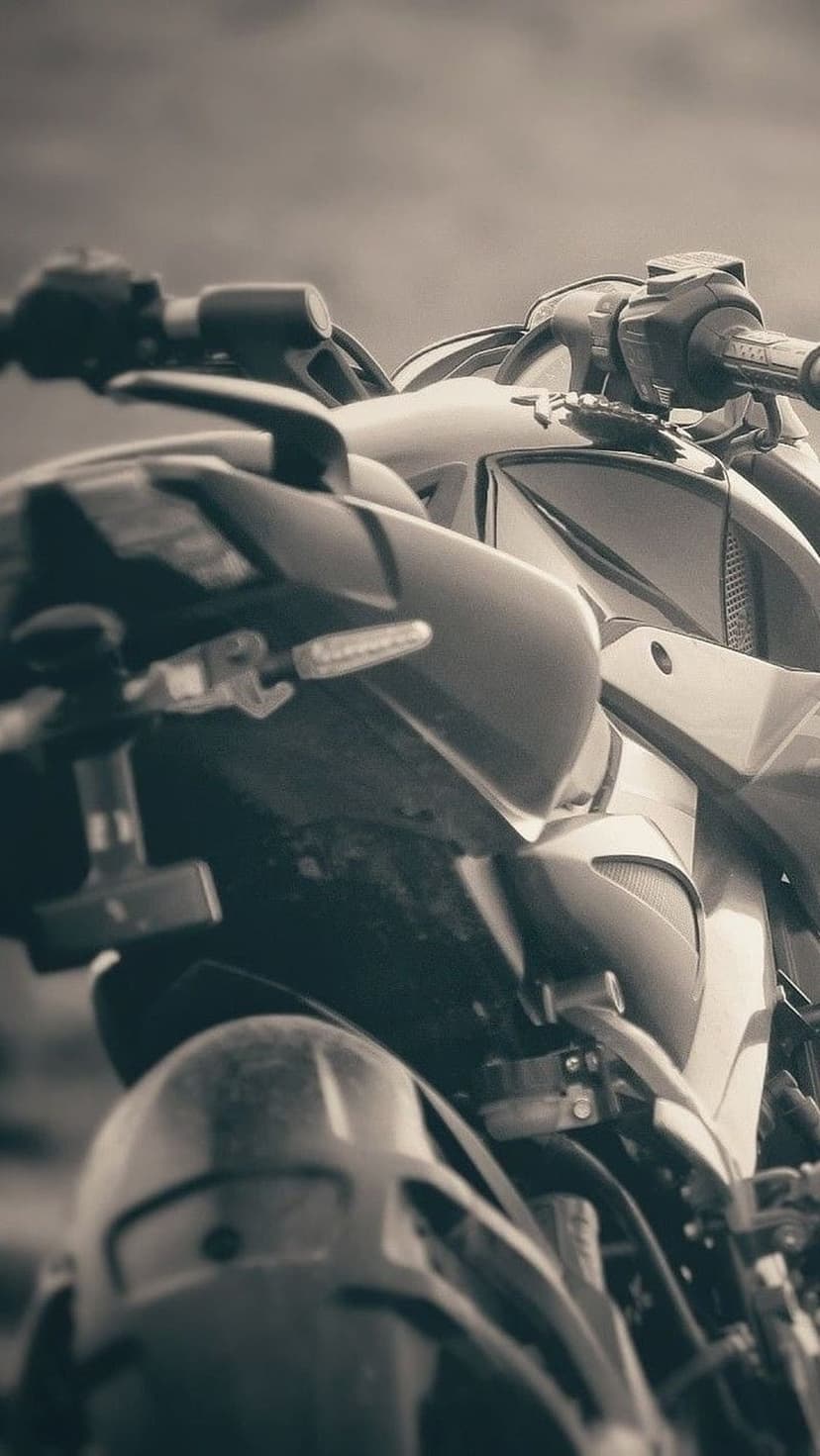 Motorcycle handlebars and metallic front fairing shown in a low-angle black and white sepia close-up shot.
