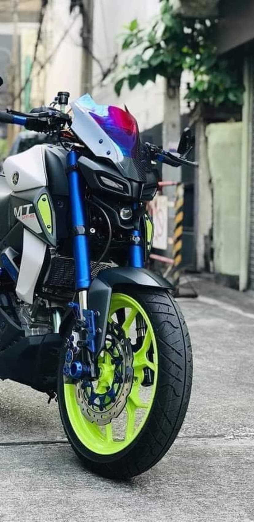 Yamaha MT-07 streetfighter with neon green rims, blue front suspension, and a colorful iridescent windshield.