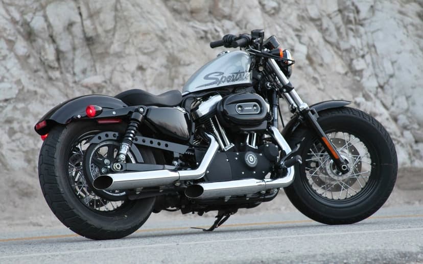 Silver Harley-Davidson Sportster 1200 with chrome exhausts parked on asphalt against a rocky cliff background.