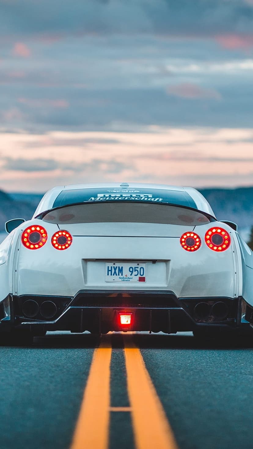 Nissan GT-R R35 rear view with glowing circular taillights on an asphalt road near distant mountains.