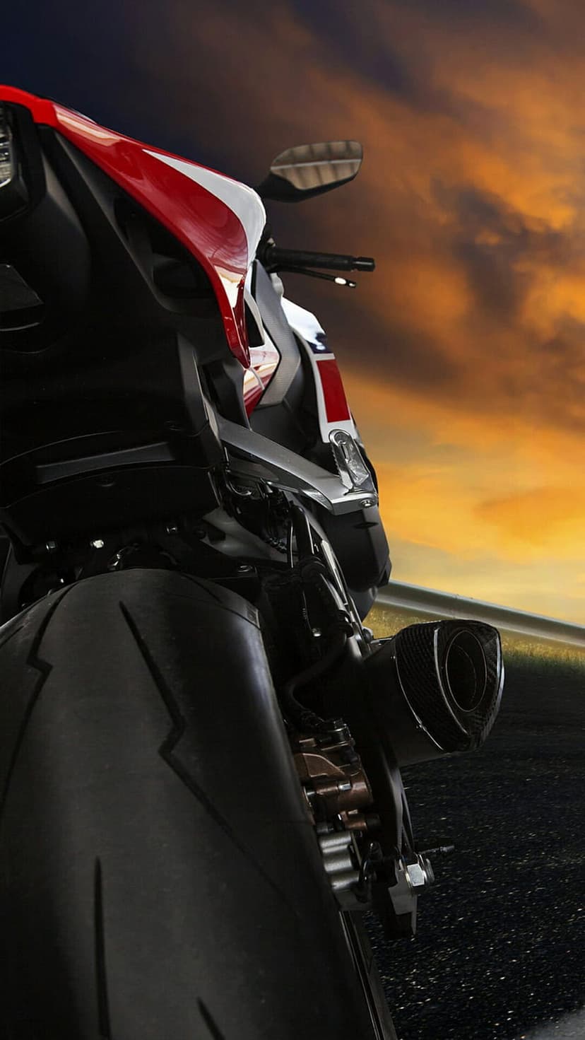 Sportbike rear tire and exhaust pipe from a low angle against a dramatic orange and grey sunset sky.