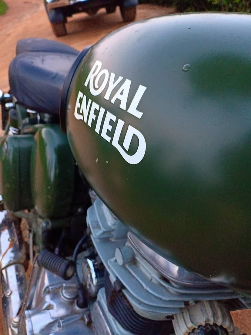 Green Royal Enfield motorcycle gas tank with a white logo, visible engine components, and a leather seat.