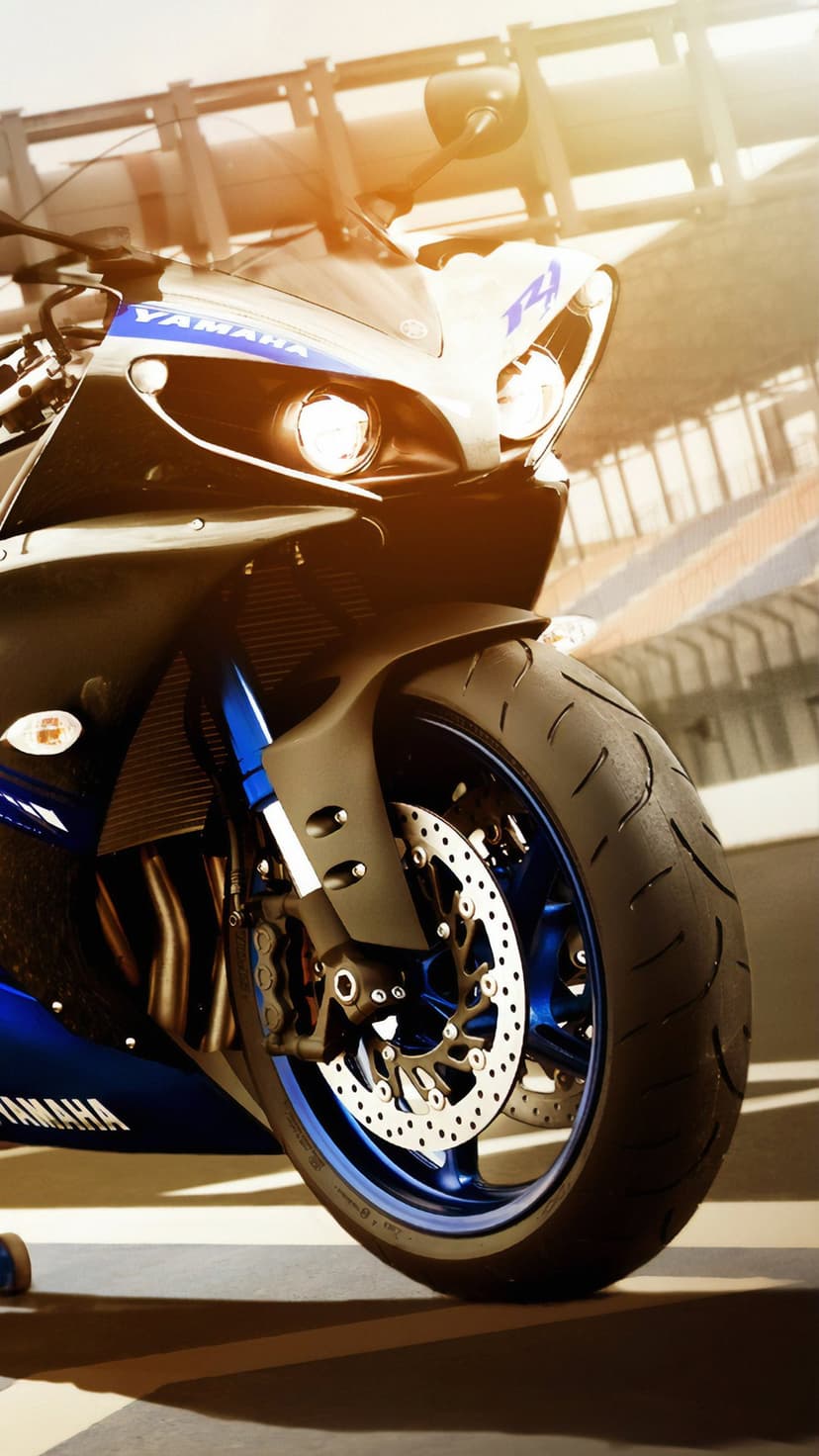 Blue Yamaha YZF-R1 motorcycle front wheel and glowing headlights with a golden sunlight flare in a race track setting.