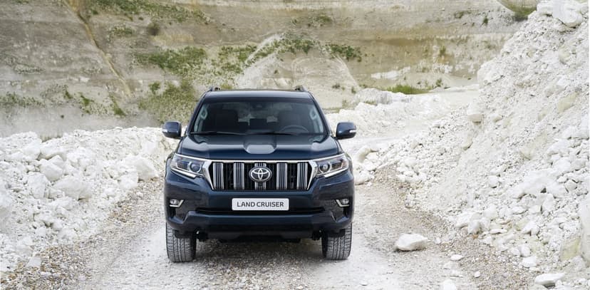 Dark blue Toyota Land Cruiser parked on a white gravel path between rocky hills in a quarry landscape.