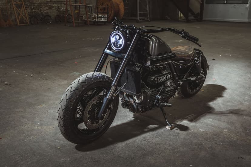 Black custom motorcycle with a glowing LED headlight parked on a concrete floor in a dark warehouse.