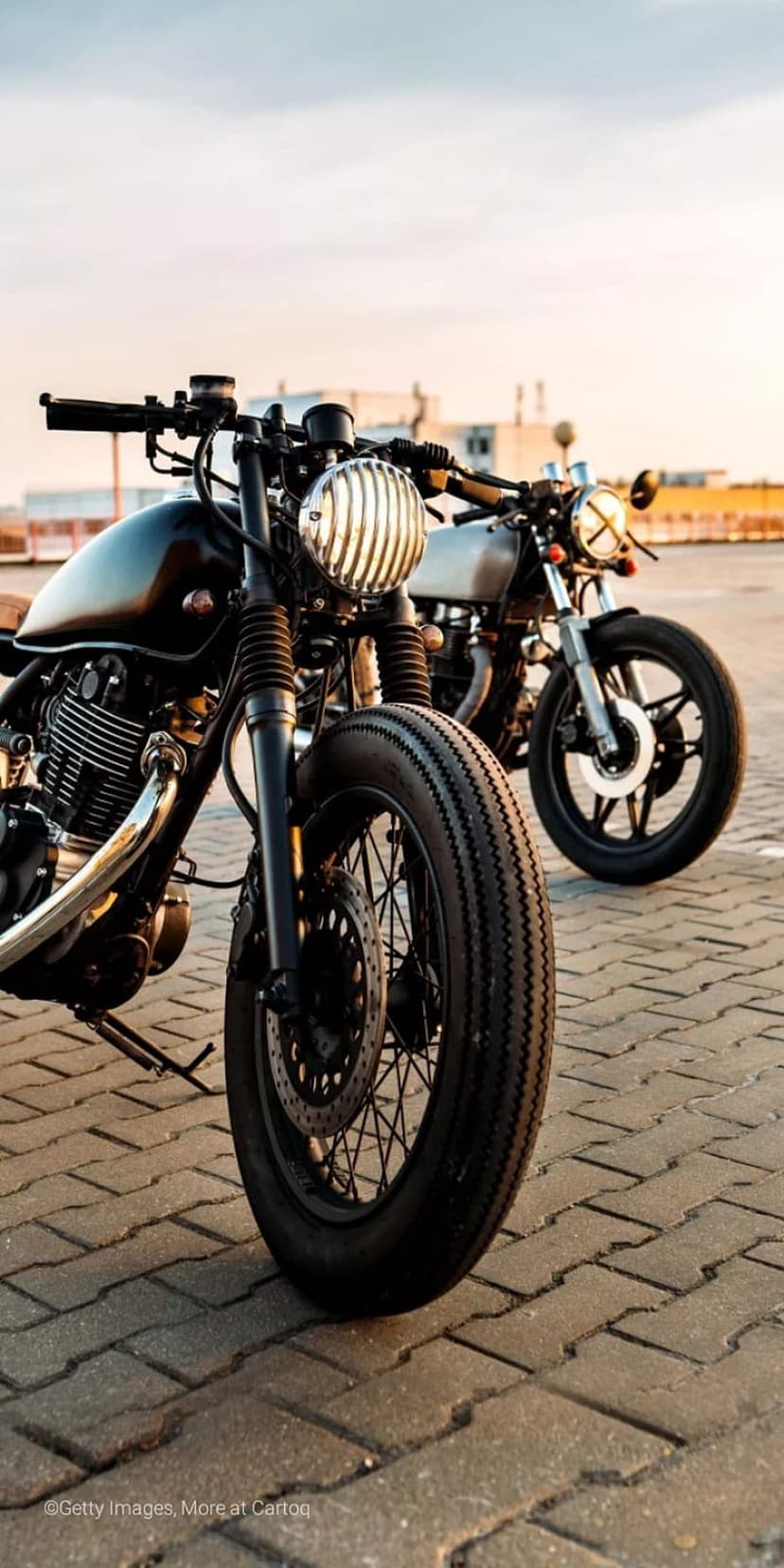 Black cafe racer motorcycle with a ribbed headlight and chrome details parked on pavement at sunset.