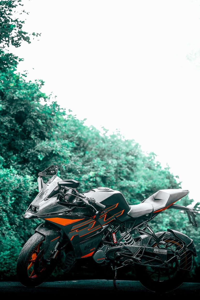KTM RC 390 sportbike featuring orange accents parked in a dense green forest with soft natural lighting.