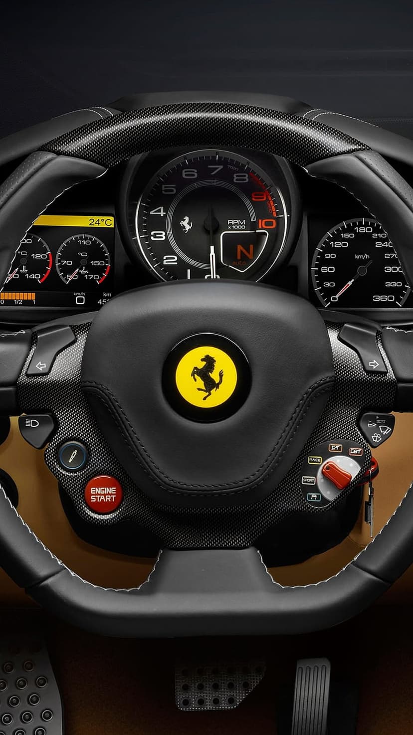 Ferrari steering wheel with yellow prancing horse emblem, red start button, and carbon fiber interior trim.