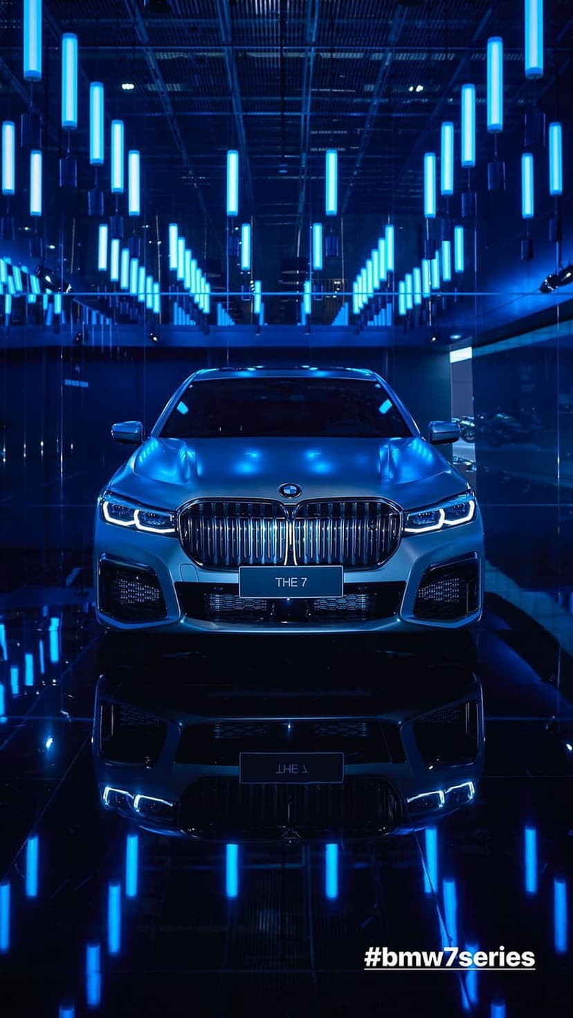 BMW 7 Series sedan with glowing blue neon light reflections on its silver metallic exterior and front grille.