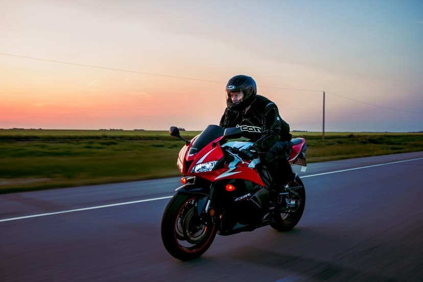 Motorcyclist on a red sportbike rides along an open highway under a vivid orange and blue sunset sky.