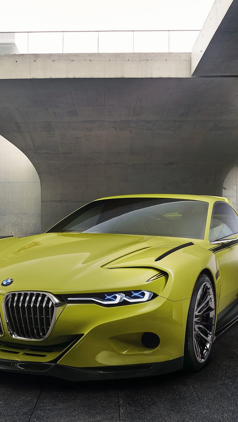 Lime green BMW concept car with sharp LED headlights parked in a brutalist concrete architectural setting.