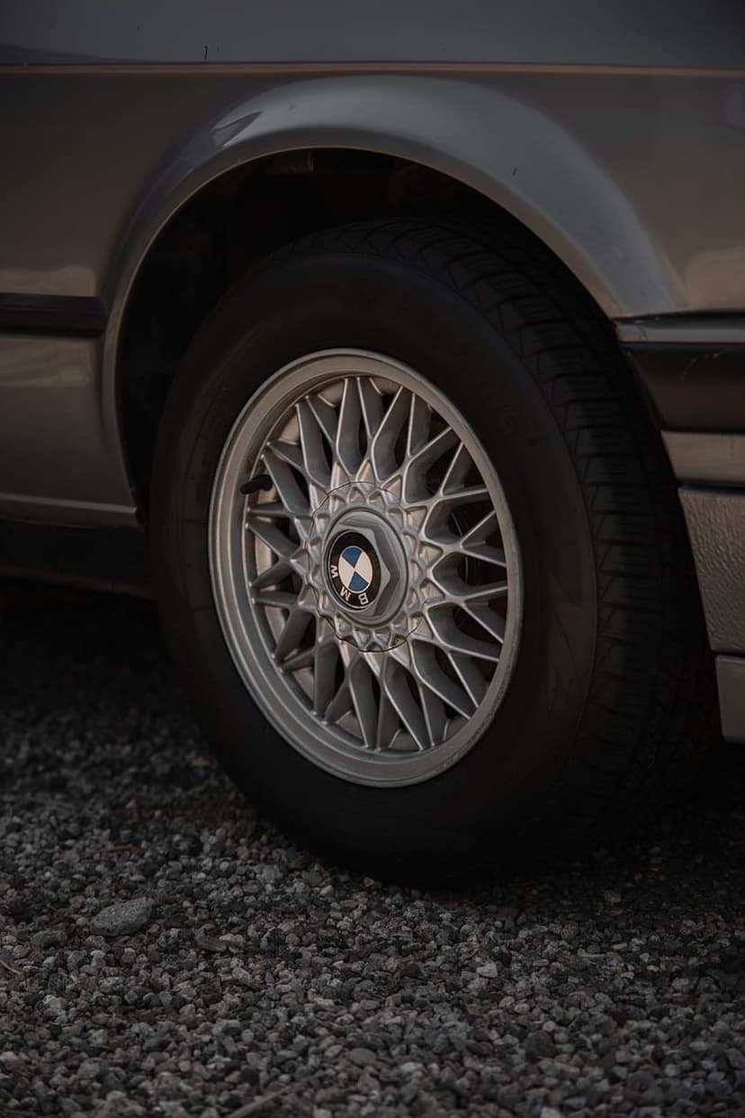 BMW star-spoke alloy wheel with a central logo sits on a gravel surface against a metallic gray car body.