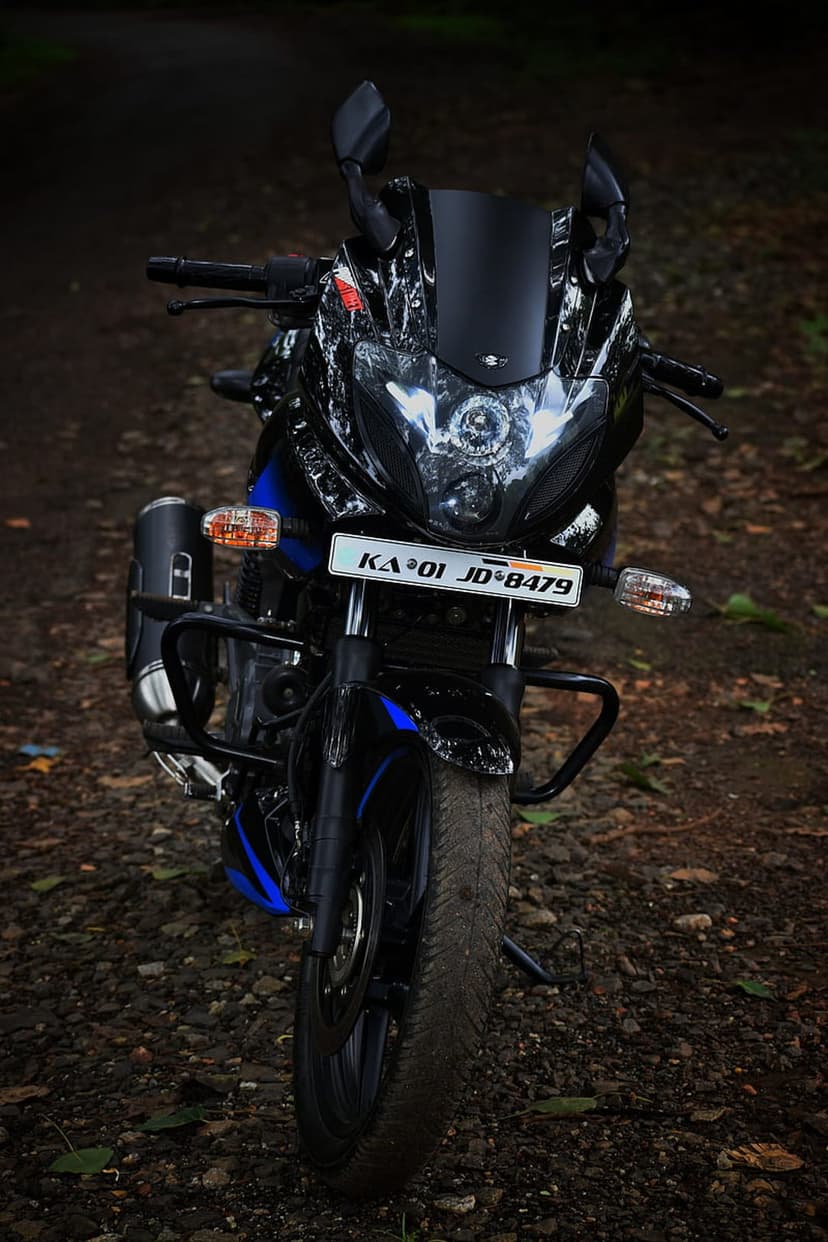 Pulsar 220F motorcycle with dual headlights and blue accents parked on a dirt path in a vertical orientation.
