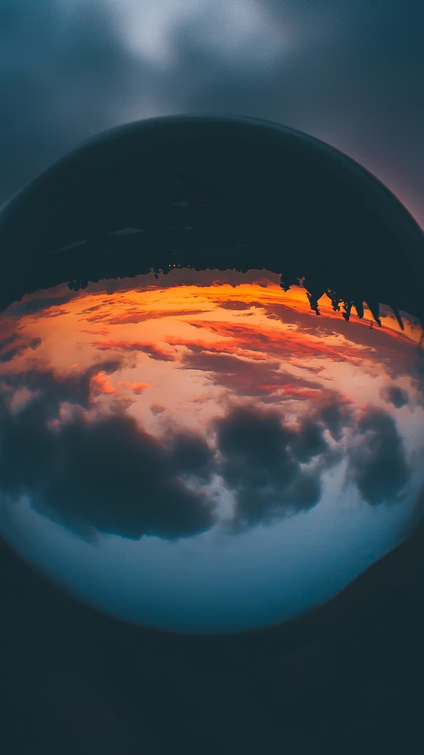 Clear glass sphere containing an inverted reflection of orange sunset clouds against a blurred horizon backdrop.