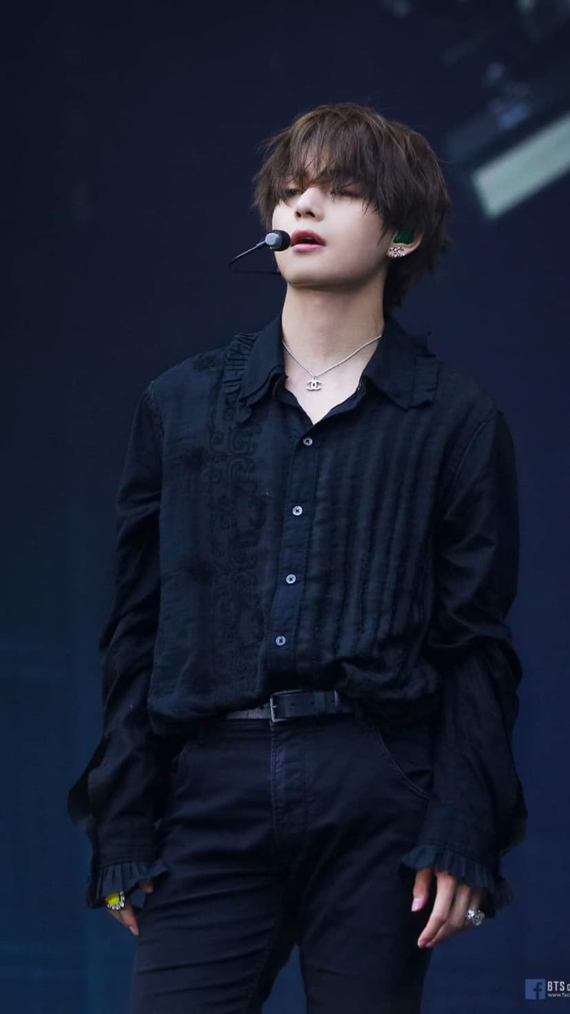 Kim Taehyung performs in a black ruffled shirt and silver necklace during a moody stage concert production.