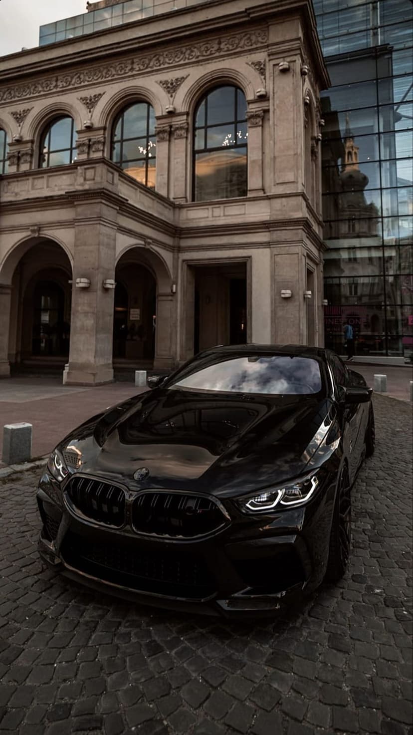 Black BMW M Series sports car featuring a glossy finish and LED headlights on a historic cobblestone street.