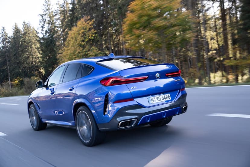 Blue BMW X6 M50i SUV driving on a highway through a forest with dynamic motion blur and sunlight.