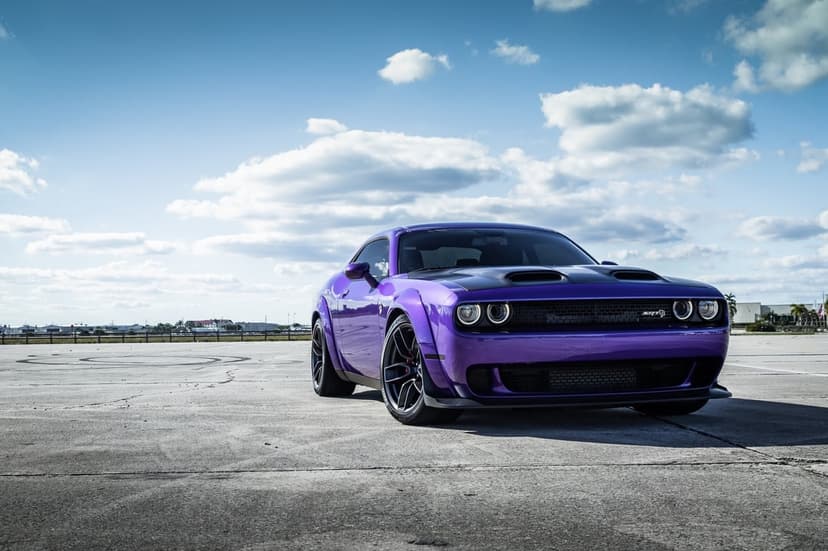 Purple Dodge Challenger SRT Hellcat Widebody parked on an asphalt track under a bright blue sky with clouds.