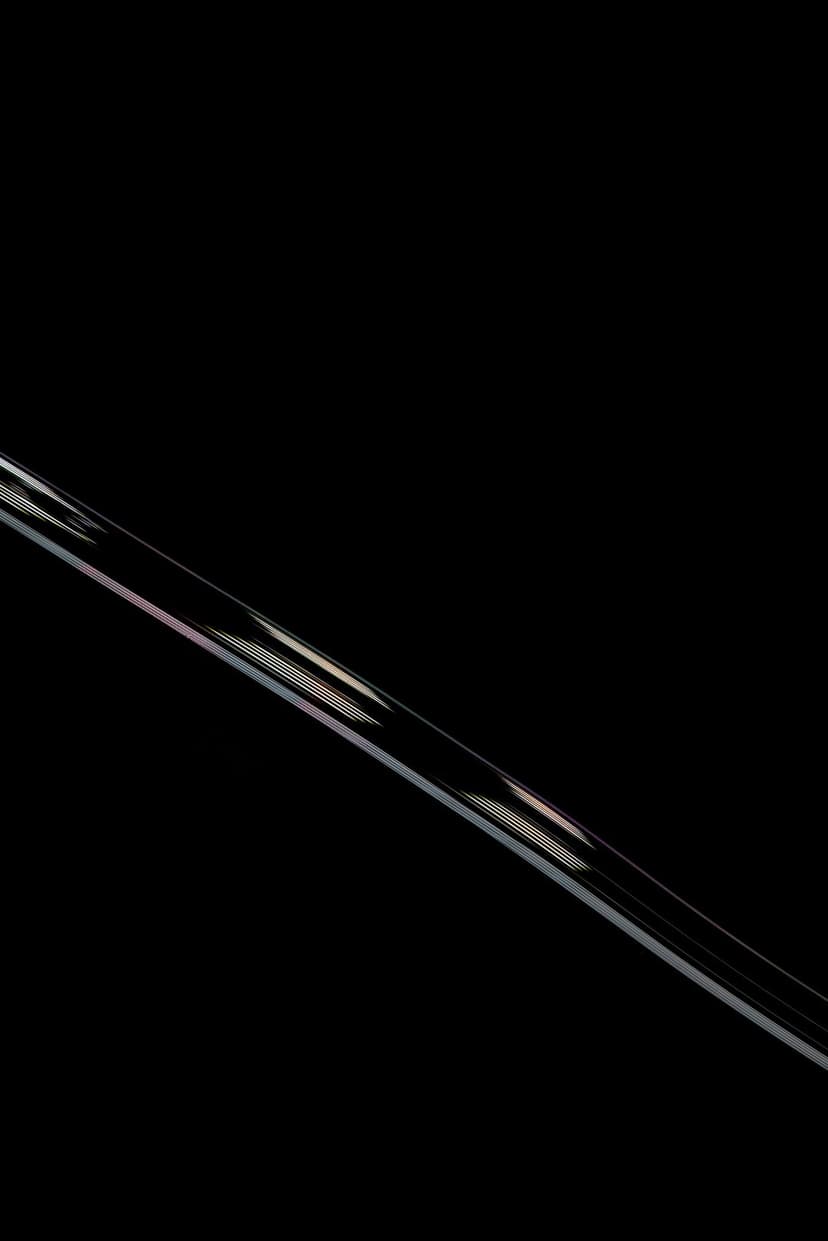 Diagonal rainbow light beam with iridescent edges cutting across a solid matte black vertical background.