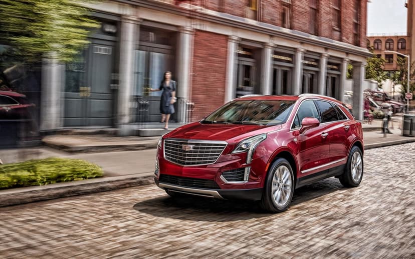 Red Cadillac XT5 SUV moving along a cobblestone street past historic brick buildings with motion blur.