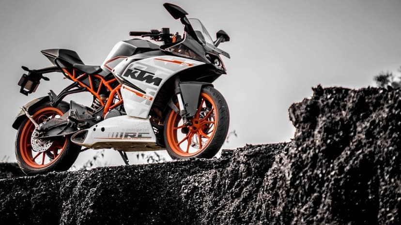 White and orange KTM RC 390 sportbike on a dark rocky mound under a bright desaturated sky.