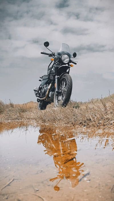 Motorcycle Reflection in Puddle on Grassy Terrain