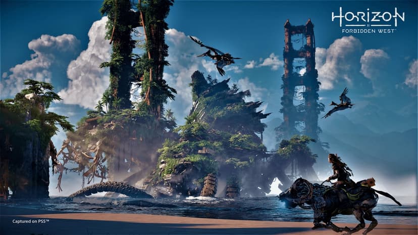 Aloy rides a mechanical creature on a beach near overgrown ruins of the Golden Gate Bridge under a blue sky.