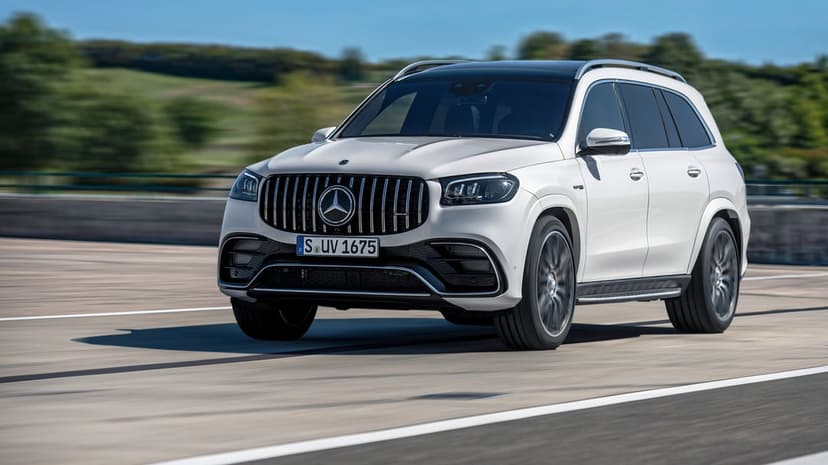 White Mercedes-AMG GLS 63 SUV driving fast on a track with motion blur and clear blue sky background.