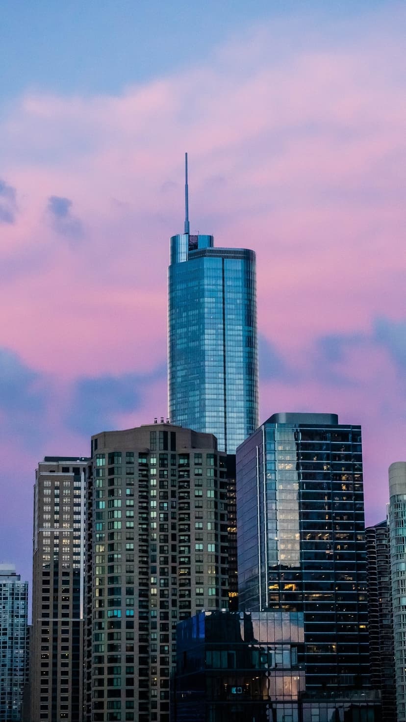 Illuminated urban skyline sits beneath a dramatic magenta to teal gradient sky during a serene twilight evening.
