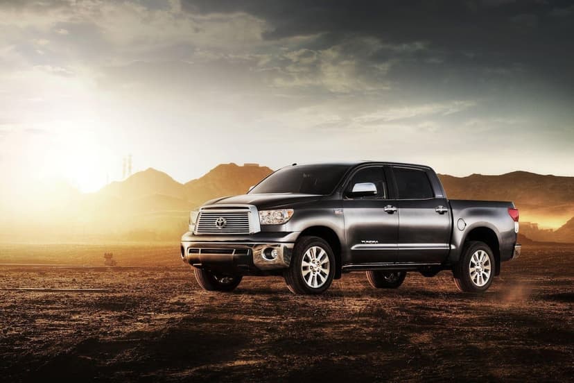 Charcoal grey Toyota Tundra Platinum truck parked on dry desert ground during a hazy mountain sunset.