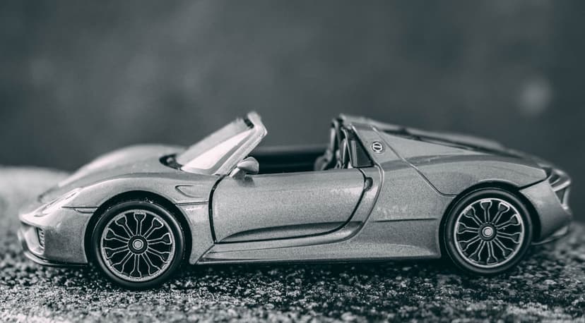 Silver convertible sports car model on a bed of gravel with a blurred background and detailed wheel rims.