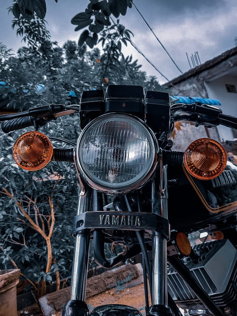 Vintage Yamaha motorcycle front view showing a round glass headlight, orange turn signals, and a chrome emblem.