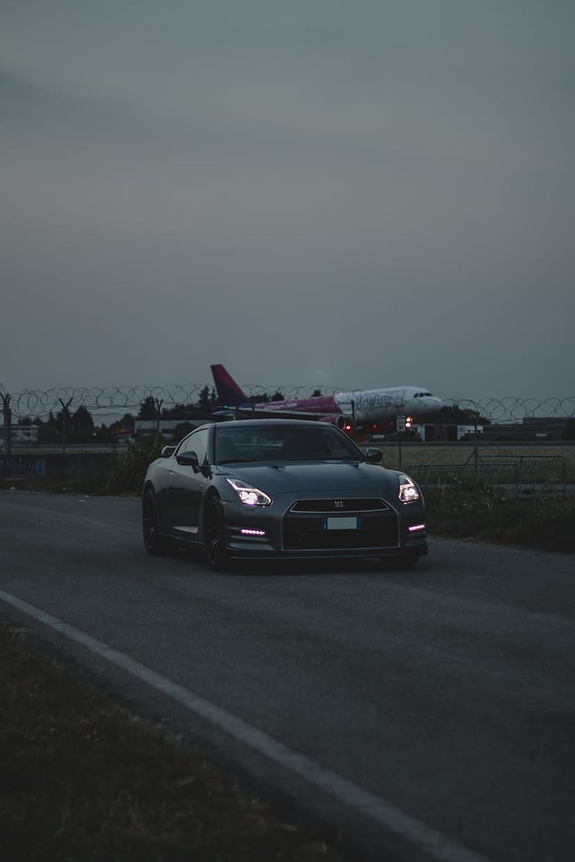 Nissan GT-R sports car in motion at an airport during dusk with a parked airplane in the background.