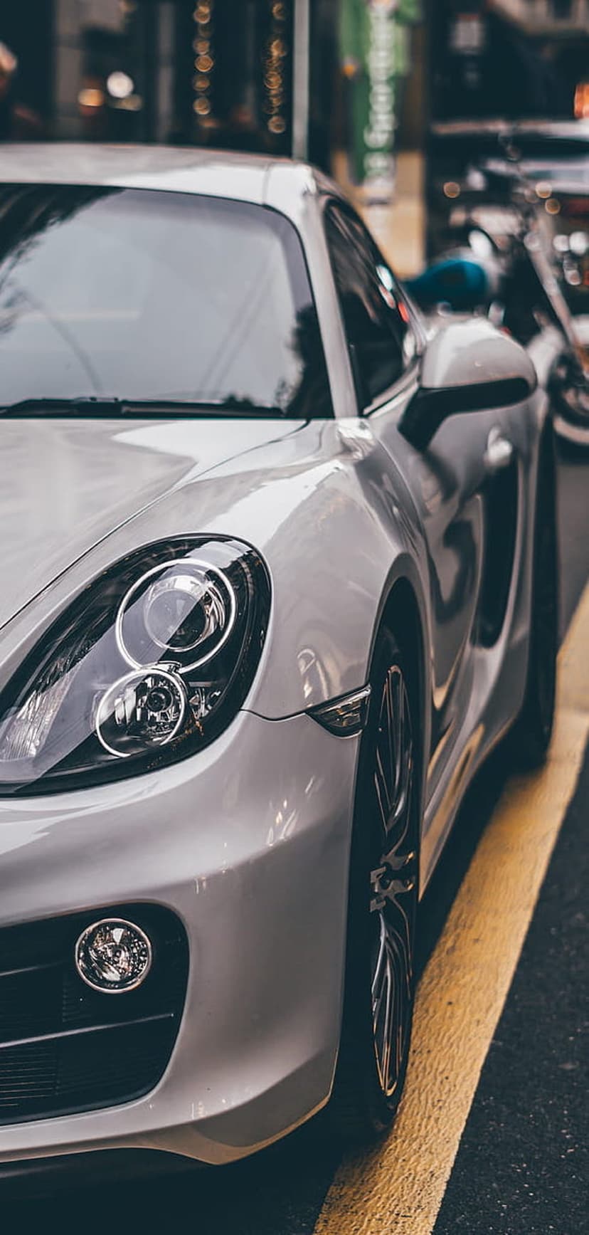 Silver Porsche Cayman with round headlights and metallic body parked on a dark city street with yellow road lines.