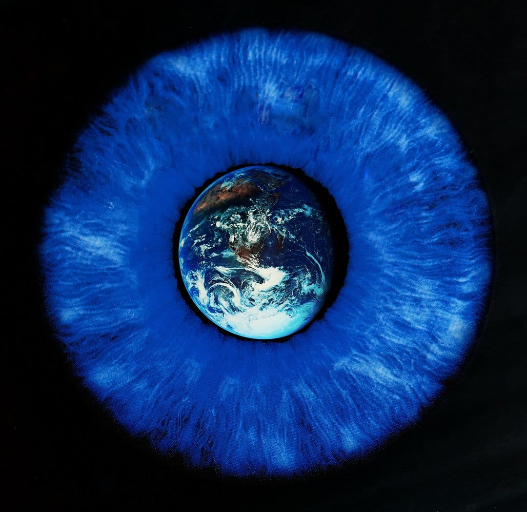 Planet Earth with visible continents and white clouds sits inside the pupil of a detailed blue human eye.