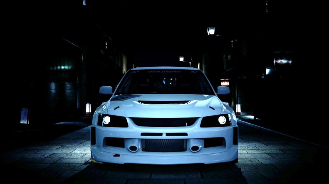 White modified Mitsubishi Lancer Evolution parked on a dark narrow street with dramatic cinematic lighting.