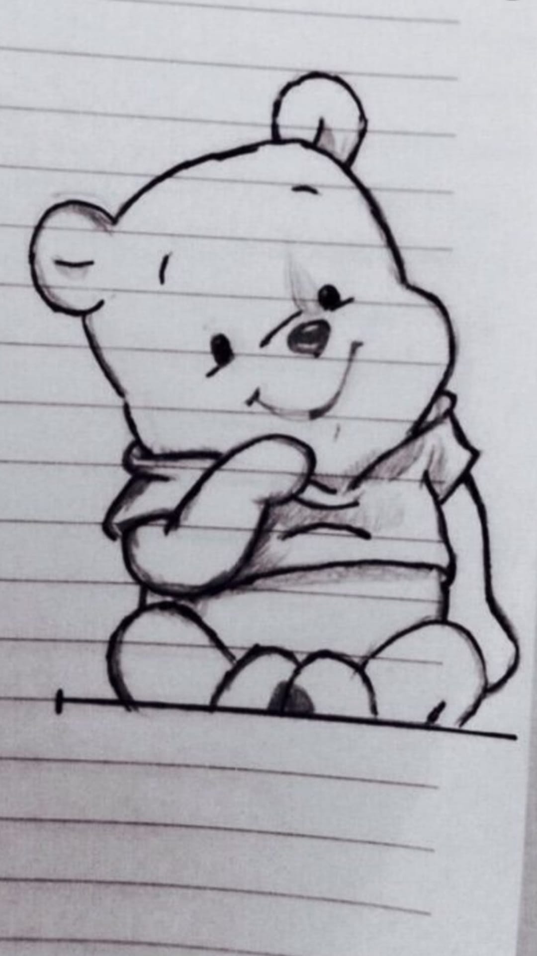 Winnie the Pooh sits smiling while wearing a scarf in a pencil drawing on a page of lined notebook paper.