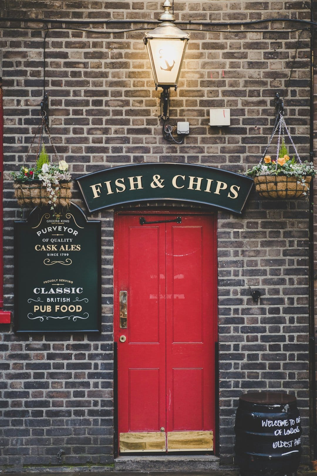 Red double door of a classic British pub with hanging flower baskets and a hand-written fish and chips sign.