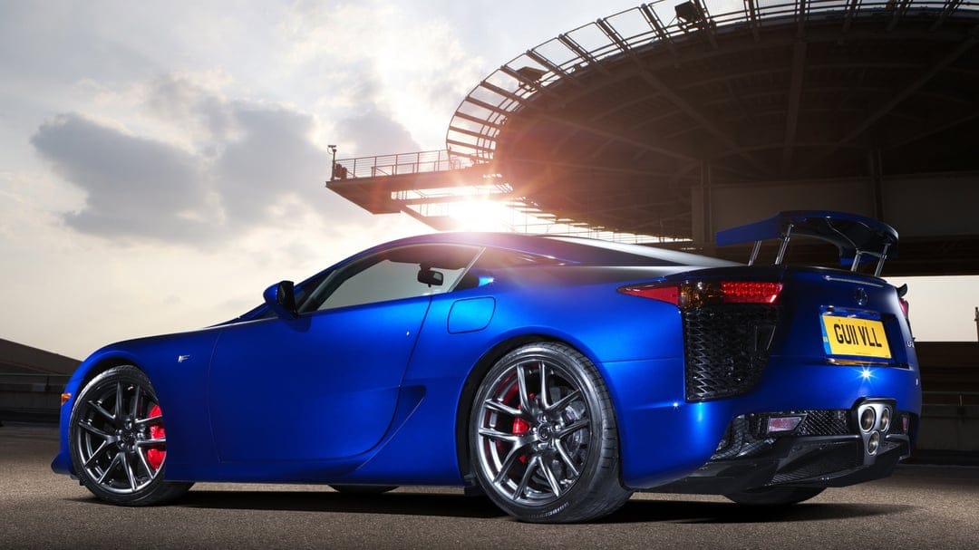Blue Lexus LFA supercar parked under a circular structure at sunset with red brake calipers and triple exhaust.