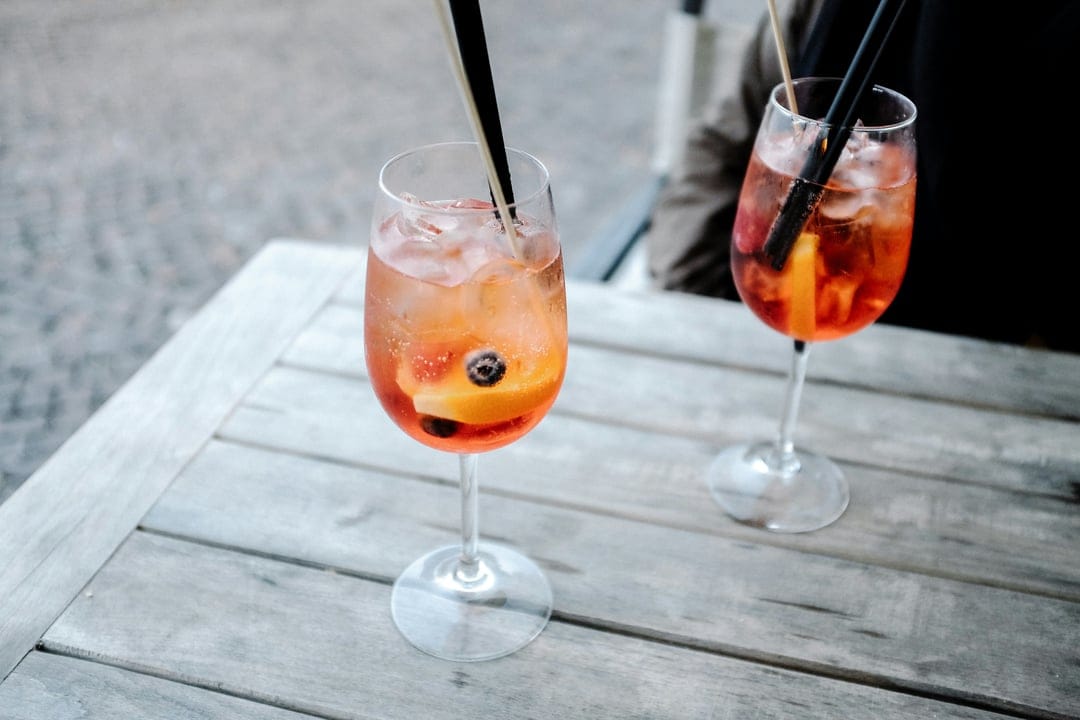 Two Aperol Spritz glasses with orange slices and blueberries on a wooden table with a soft blurred background.